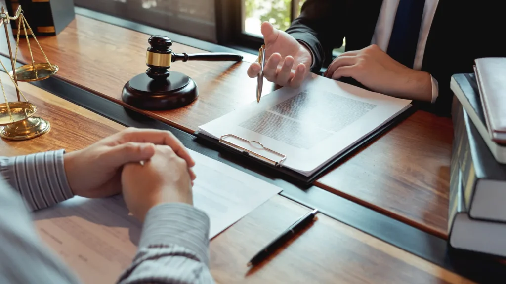 A lawyer and client discuss documents at a desk, with a gavel prominently placed nearby.