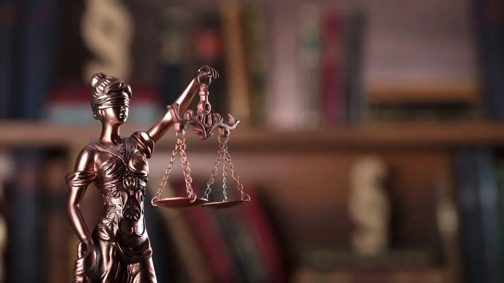 Close-up of a Lady Justice statue with scales in front of law books.